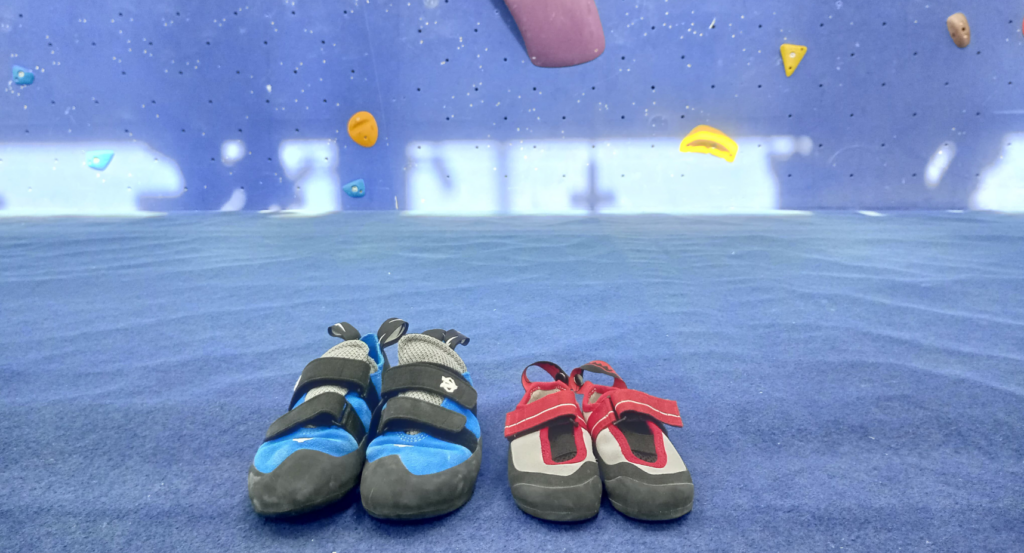 A pair of adult climbing shoes and a pair of childrens' climbing shoes on a blue bouldering mat