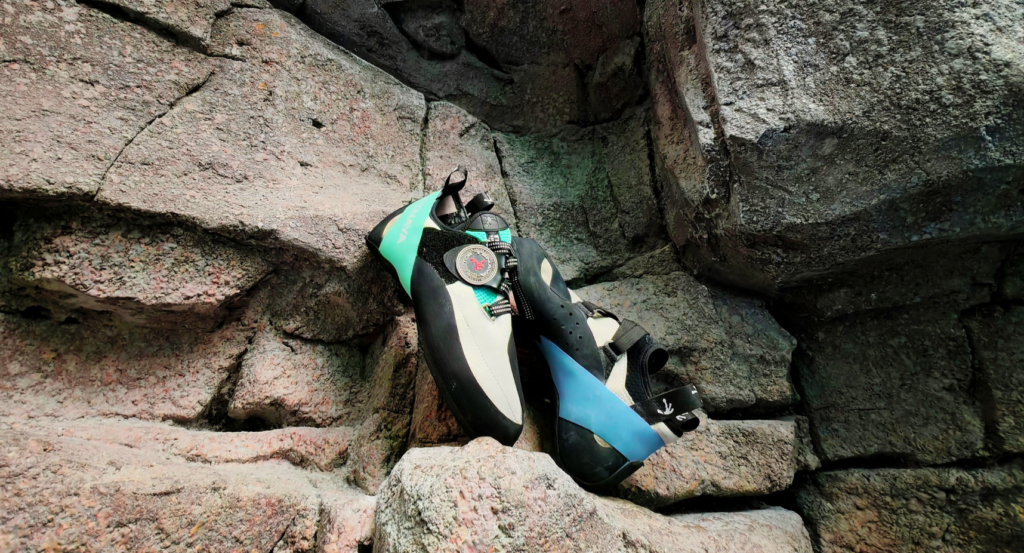 A pair of blue and white Tenaya climbing shoes on a grey rock face
